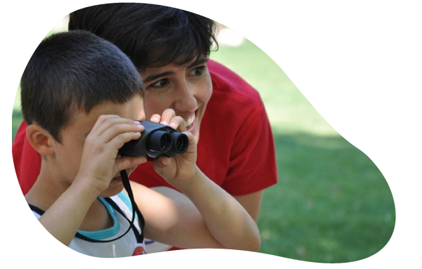 Niño mirando con prismáticos, acompañado de un adulto, en el campo