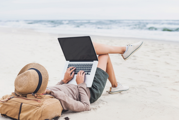 Una persona tumbada en una playa, en la arena, escribiendo en un ordenador